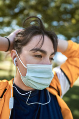A beautiful white woman with brown hair and a sports suit with a yellow jacket prepares for exercise and exercises her muscles to avoid cramps in a park near the city wearing a Covid 19 mask     