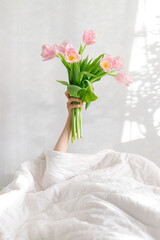 good morning pink tulips in a woman's hand in bed, birthday greetings, international women's day, valentine's day, gift, flowers, pink bouquet, spring tulips, surprise