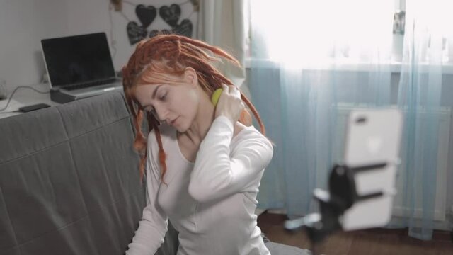 A woman blogger with red dreadlocks recording video or live broadcast using smartphone and tripod at home.Online show On-air production host streaming live content, recording digital social media