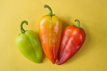 green, orange and red bell peppers isolated on yellow background . High quality photo