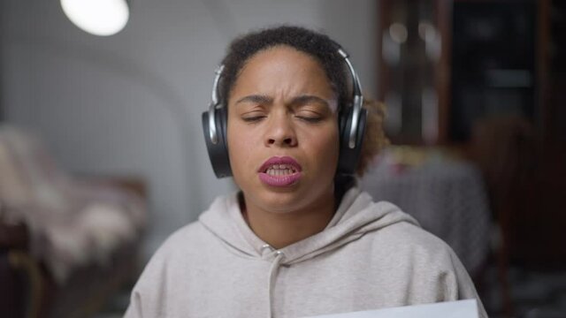 Video call POV of desperate African American young woman in headphones talking justifying herself for strategy failure. Unsuccessful beautiful employee in web conference from home office