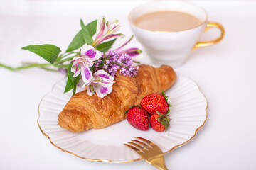 Coffee cup and sweet croissant with fresh strawberry on white table, decorated with beautiful flower bouquet