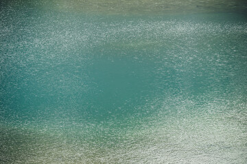 Obraz premium Texture of green blue calm water of lake. Meditative ripples on water surface. Nature minimal background of green blue lake with golden shine. Natural backdrop of lake fragment with clear azure water.