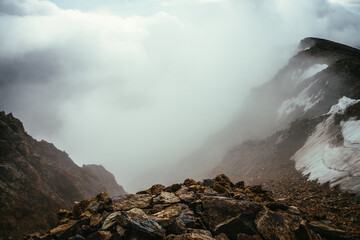 Atmospheric scenery on top of mountain ridge with snow above thick low clouds. Minimalist view from precipice edge over clouds. Beautiful minimal alpine landscape with mountain range over dense clouds