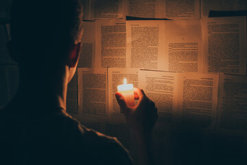 Homme mystérieux avec une bougie dans ses mains contre un mur à partir des pages d'un livre - obrazy, fototapety, plakaty