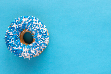 Donut with blue and white sprinkles on blue background with copy space.