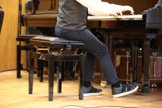 A boy plays the piano while sitting on a chair in a classroom at a lesson. The feet of a child in jeans and sneakers press the pedal. Image of school educational process
