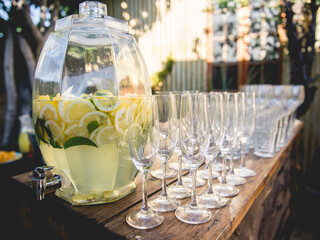 Large glass jug with natural homemade lemonade and glasses on wood table in the garden with beautiful sunlight