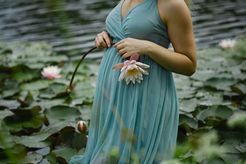 Sensual pregnant women in blue dress holding water lilly in hands.