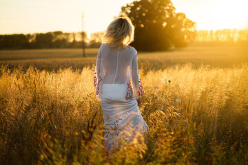 Beautiful blond women in a white dress in nature in the summertime. View as the symbol of freedom and youth.