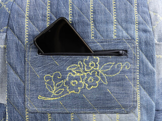 pocket of bag made of denim with smartphone inside, which is visible from an unzipped zip fastener, close-up