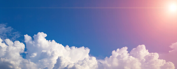 Blue sky background with white puffy clouds on a bottom foreground. Panorama with fluffy clouds and...