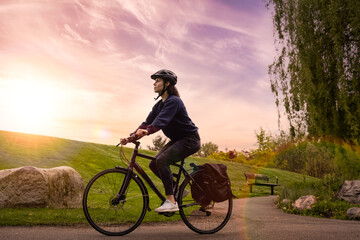 Obraz premium Adult Caucasian Woman Riding a Bicycle on a path in a modern city park. Sunset Art Render. Taken in Hawthorne Rotary Park, Surrey, Vancouver, British Columbia, Canada.