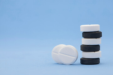 Pharmaceutical medical set of white and black pills stacked in the form of a tower on a blue background with copy space. Prescription medicine, antibiotic concept in round tablets with space for text.