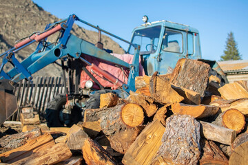 a pile of sawn wood, chocks, lies in the yard on the street in the village against the background of an old tractor