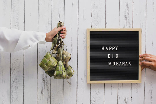 Hand holding rice cake in Indonesia called ketupat and letter board says Happy Eid Mubarak