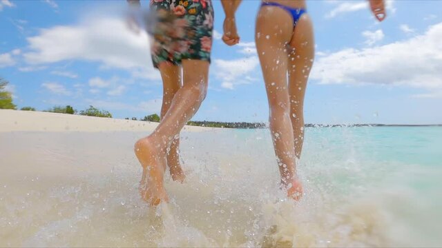 Back view of unrecognizable couple running on seashore and splashing water over camera. Slow-motion
