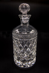 Empty crystal decanter with engraving, Closed with a glass stopper on black background. Selective focus.