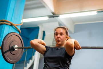 Fototapeta na wymiar young latina female athlete doing crossfit and lifting a weighted barbell at the gym