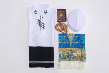 Flat lay of Muslim traditional dress and accessories for praying with Holy Book Al Quran and praying beads. There is Arabic letter which means the holy book