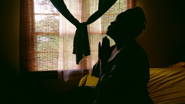 Black female sitting on bed on a cloudy day praying and talking to God