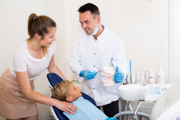 Obraz premium Stomatologist in uniform is telling to young boy and mother about healthcare in clinic.