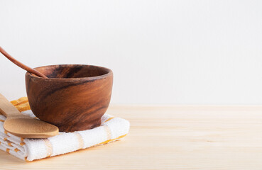 Wooden kitchen utensils on table. Bowl, spoons and towel on white wall background. Home cooking, culinary concept. Copy space