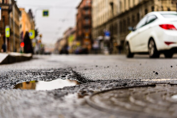 Rainy day in the big city, the cars drive along the old road. Close up view of a hatch at the level of the asphalt
