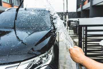 The young man washed the car by using a hose to spray water over the car. The water spreads all...