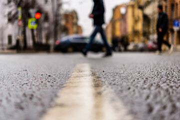 Rainy day in the big city, the pedestrians cross the road. Close up view from the level of the dividing line