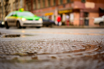 Rainy day in the big city, the cars stand at the crossroads. Close up view of a hatch at the level of the asphalt