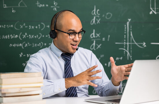 Indian young teacher man sitting wearing headset teaching online video conference live stream by laptop. Asian teacher teaching mathematics class webinar online for students learning.