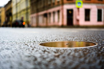 Rainy day in the big city, the empty road between houses. Close up view of a hatch at the level of the asphalt