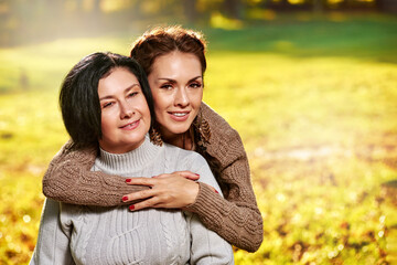 Fototapeta premium Portrait of smiling beautiful woman hugging her happy mom in autumn park