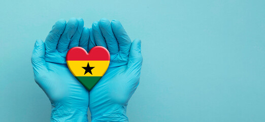 Fototapeta premium Doctors hands wearing surgical gloves holding Ghana flag heart