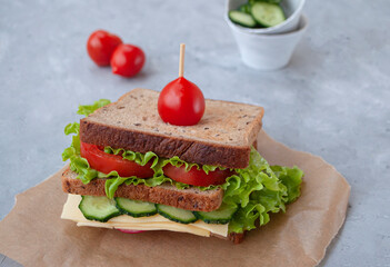Delicious sandwich with fresh lettuce leaves, tomatoes, cucumbers and cheese on a grey table background.