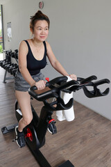 Beautiful attractive middle age southeast Asian woman exercising stationary bicycle cycle bike in a gymnasium healthy lifestyle look forward