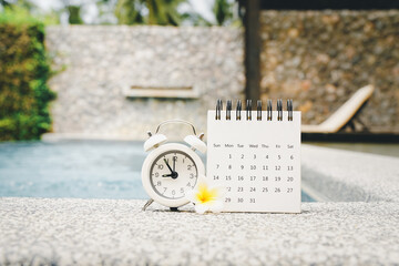 white analog alarm, opened calendar and blooming plumeria flower on concrete floor with blurred...
