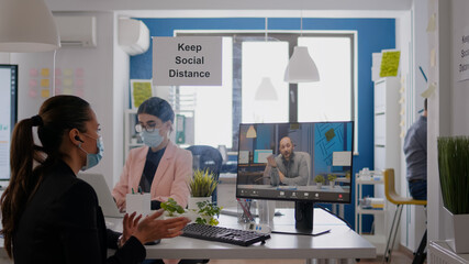 Coworkers wearing medical face masks to prevent infection with coronavirus while working in office company. Business woman talking with her team during online communication meeting