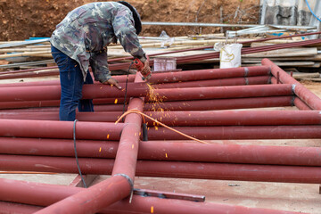 Construction workers are using grinding machines on large steel pipes. Used as a roof pole....