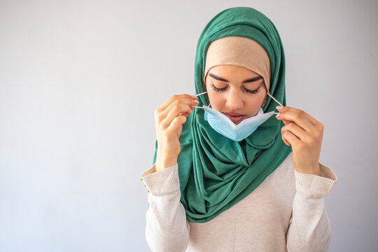 Young Muslim woman takes off medical mask. Isolated on grey background. Health care and medical concept. Close up portrait. Woman taking off her medical mask, portrait