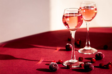 two glasses of pink gin or vodka infused with cranberry among frozen berries, cherry liqueur or any red alcoholic cocktail closeup, a pair of long-stemmed glasses, copy space