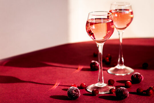 two glasses of pink gin or vodka infused with cranberry among frozen berries, cherry liqueur or any red alcoholic cocktail closeup, a pair of long-stemmed glasses, copy space