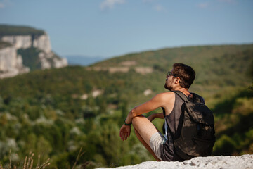 Naklejka na ściany i meble Young male hiker with backpack relaxing on top of a mountain during calm summer sunset
