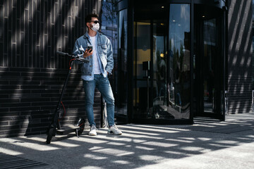 Obraz premium The guy on the electric scooter uses the phone near the office.