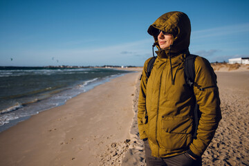 Close up handsome traveller man in winter jacket and black sunglasses walking on the sand beach in sunny winter day and ejoying the sea. Norway