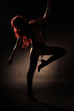 Eine rothaarige Frau posiert nackt an einer Kette im dunklen Fotostudio