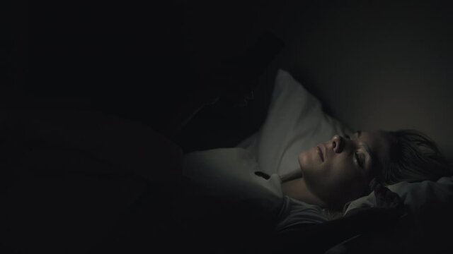 Late online. Night fatigue. Bed habit. Internet addiction. Tired exhausted woman falling asleep dropping mobile phone in dark bedroom.