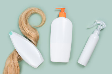 Shampoo wrapped in lock of curly blonde hair, conditioner bottle and hair spray mockups on mint background, top view. Flat lay in pastel colors. Hair care cosmetics, haircare products, hair treatment
