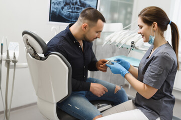 Young woman dentist selecting a shade of enamel for implantation. Male patient consults on dental treatment in a modern dental clinic